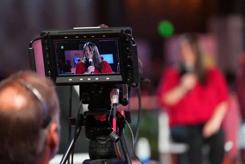 Lorena Lovric framed on a broadcast camera monitor while speaking on stage